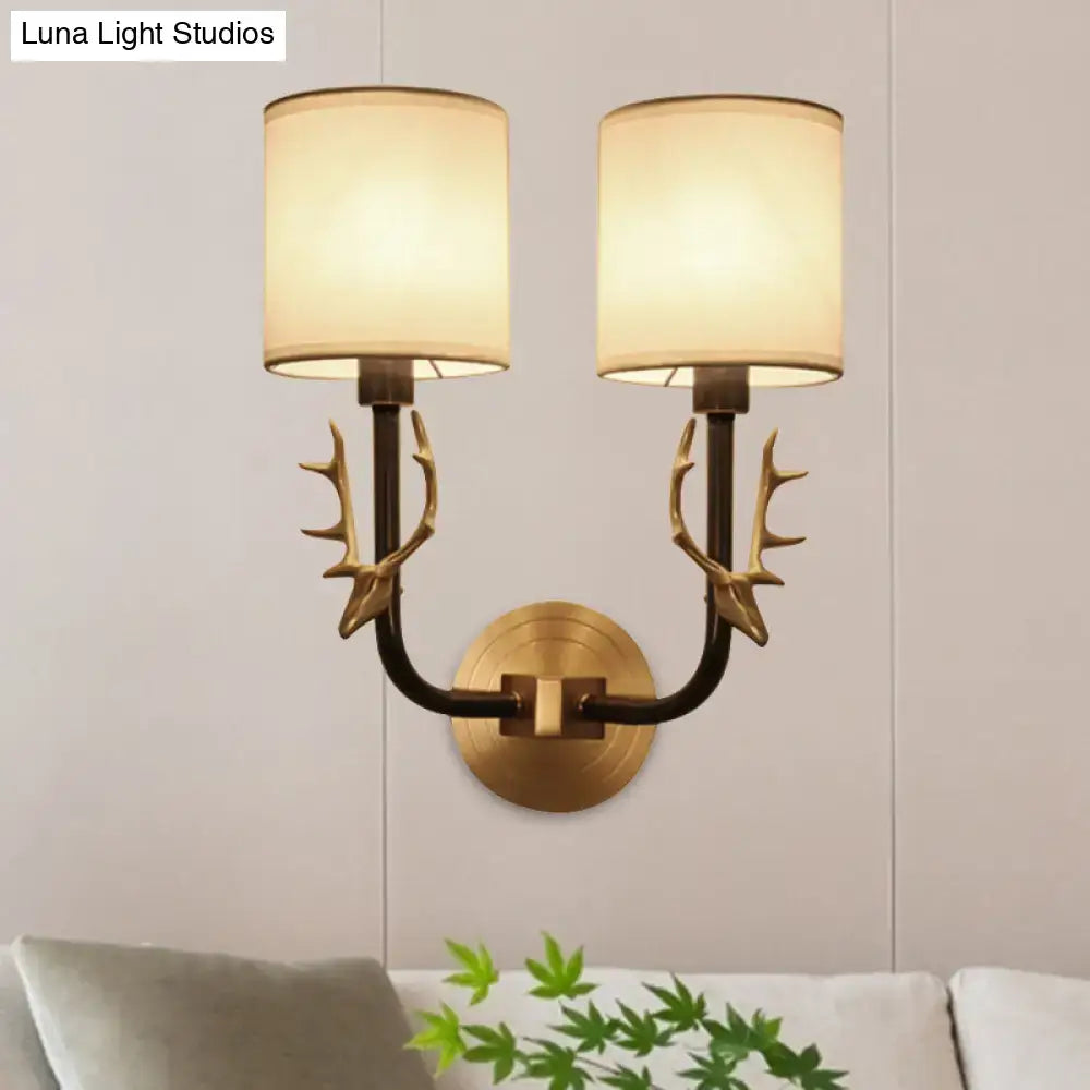 Antique brass antler wall sconce with a stylish design and two cream fabric shades for elegant bedroom lighting