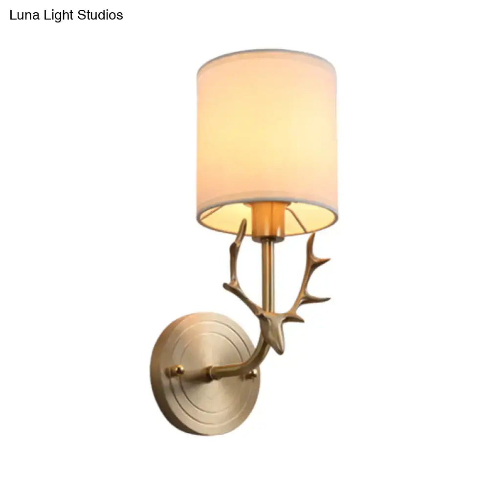 Antique brass antler wall sconce with cylindrical off-white fabric shade featuring stylish design for bedroom lighting
