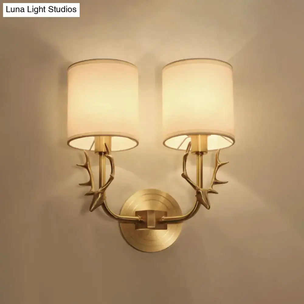 Antique brass wall sconce with gold-toned antler arms and two cylindrical cream fabric shades stylish design for bedroom light
