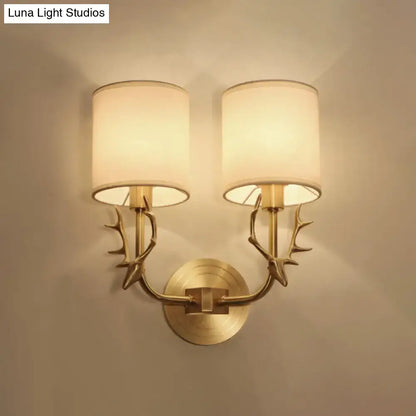 Antique brass wall sconce with gold-toned antler arms and two cylindrical cream fabric shades stylish design for bedroom light