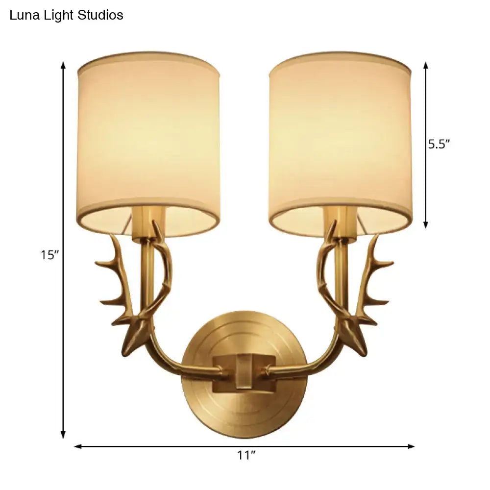 Antique brass wall sconce with stylish antler-inspired arms and matching beige fabric shades for bedroom lighting