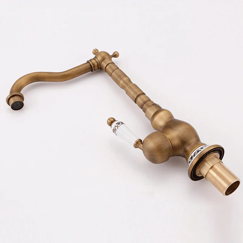 Antique brass basin faucet with curved spout and decorative glass handle featuring black floral patterns