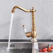 Antique brass basin faucet with a white ceramic handle featuring black decorative patterns and matching base accents