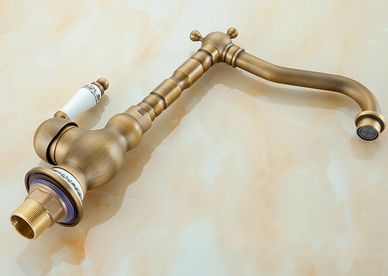 Antique brass basin faucet with a curved spout and decorative ceramic handle for kitchen use