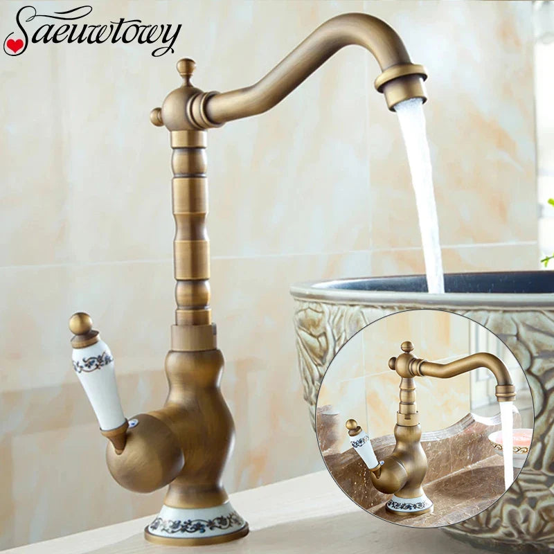 Antique brass basin faucet with curved spout and ornate segmented body featuring white ceramic handles with blue floral patterns