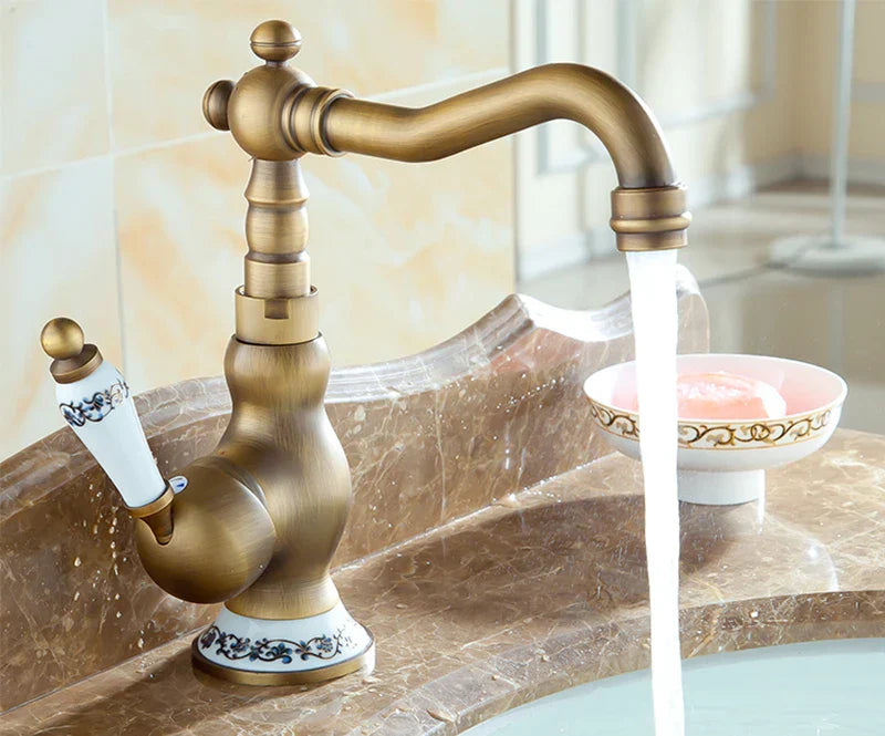 Antique brass basin faucet with ornate detailing and white ceramic handle featuring blue floral patterns