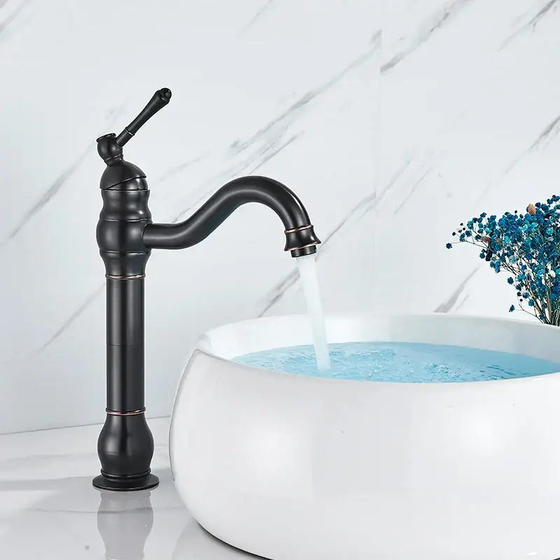 Black matte decorbites brass basin faucet with curved spout and ornate detailing beside white ceramic sink