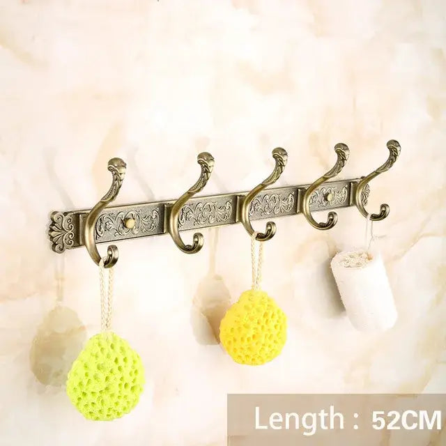 Antique brass bath hardware set featuring a wall-mounted hook rack with ornate scrollwork and five curved hooks