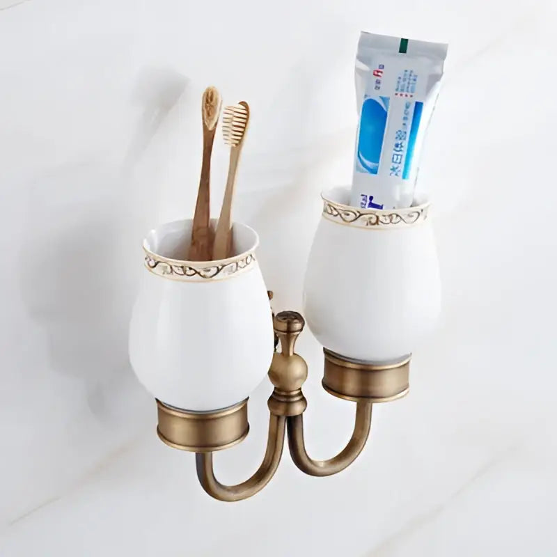 White ceramic toothbrush holder with ornate brass antique accents holding wooden toothbrushes in bath hardware set