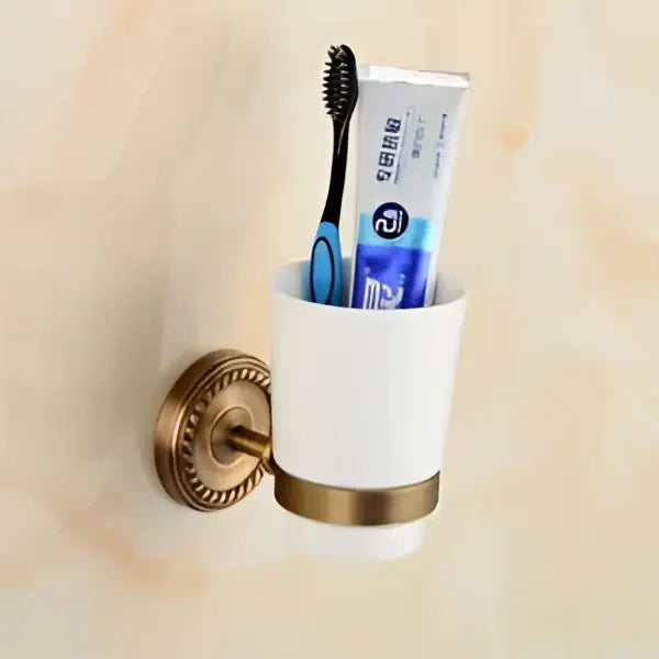 White ceramic toothbrush holder with gold-toned metal base and mounting bracket holding blue toothbrush and toothpaste decorbites brass bathroom set