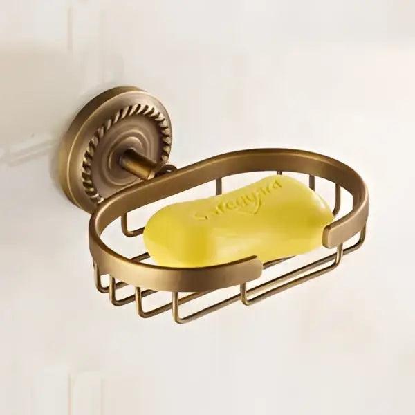 Antique brass wall-mounted soap dish with ornate mounts holding a yellow soap bar in decorbites brass bathroom set