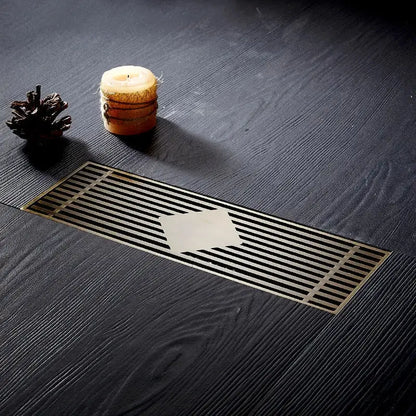 A sleek rectangular floor drain cover with a brushed metallic finish and parallel slats for bathroom deodorant use