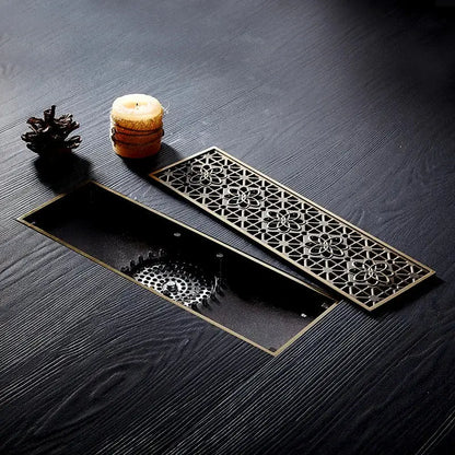 Antique brass floor drain cover with carved floral lattice design and matching removable panel for bathroom deodorant use