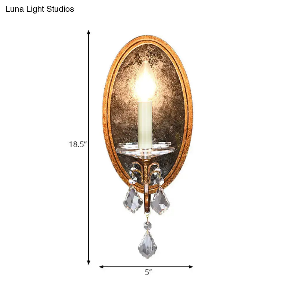 Antique brass wall sconce with antique gold finish, clear crystal droplets, mirrored back, and candle-style bulb for bedroom lighting