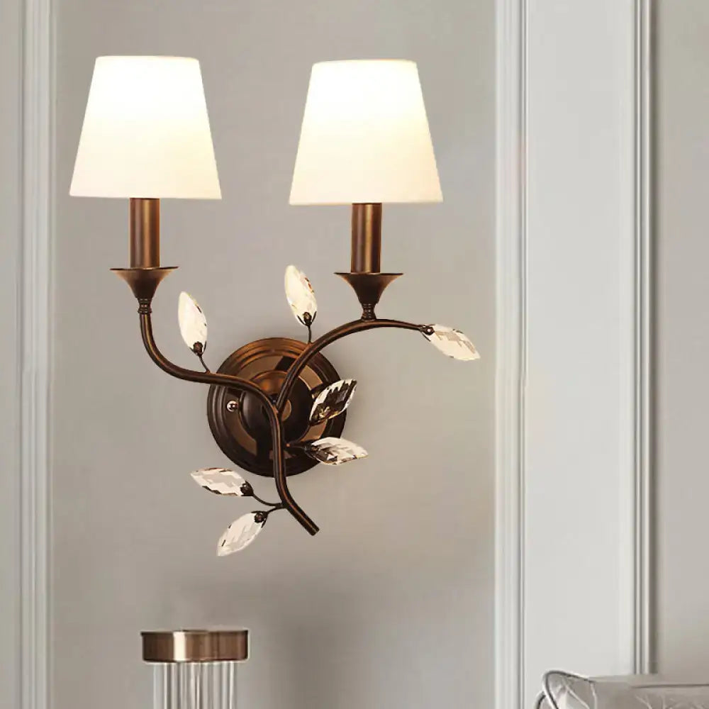 Antique brass two-light wall mount lamp with crystal leaf accents and cream fabric shades for bedroom use