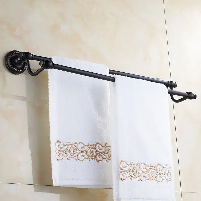 Antique brass double towel bar with ornate base in black wrought iron holding two white towels with gold embroidery