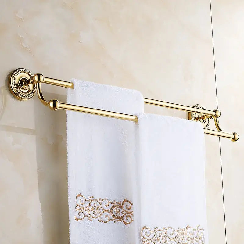 Antique brass double towel bar with gold-finished ornate circular mounts holding white towels with gold embroidery