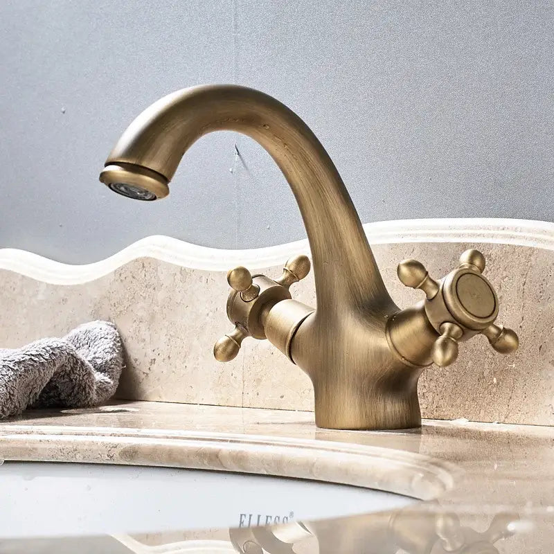 Antique brass dual handle basin faucet with vintage curved spout and ornate cross handles for bathroom vanity sink