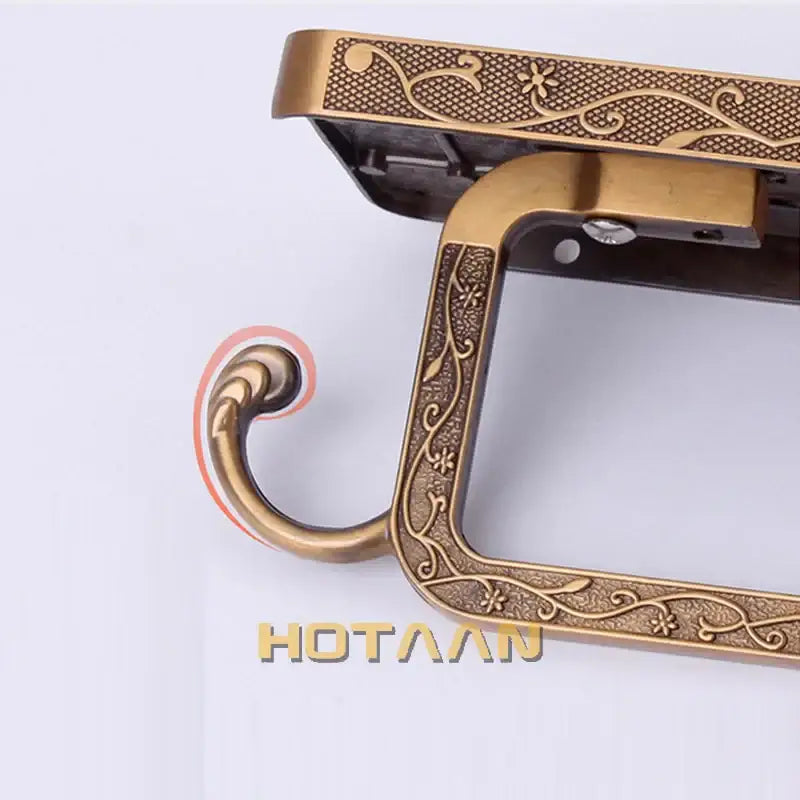 Antique brass toilet paper holder with floral and vine embossed metal frame and integrated phone rack for bathroom use