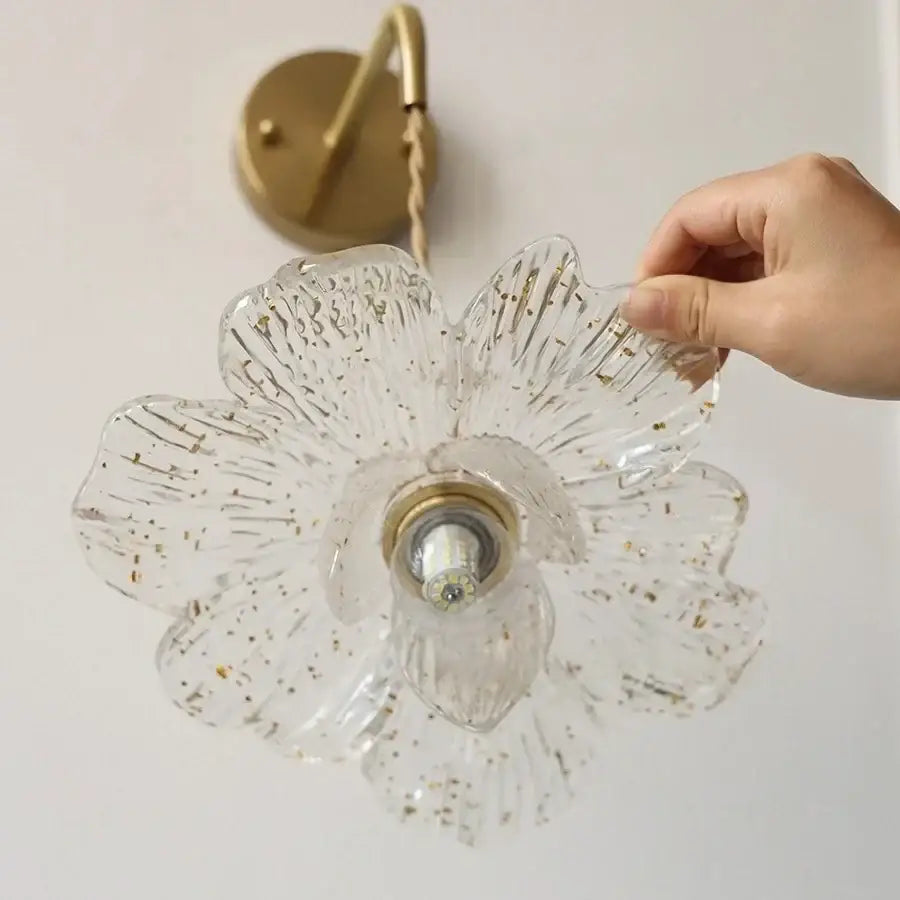 Clear glass flower-shaped led wall light with gold foil accents and antique brass mounting plate for bedroom sconce