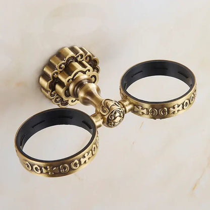 Antique brass antique glass cup holder set featuring double towel ring with ornate scrollwork and black rubber lining