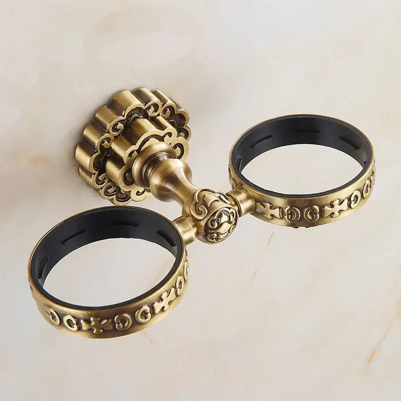 Antique brass antique glass cup holder set featuring double towel ring with ornate scrollwork and black rubber lining