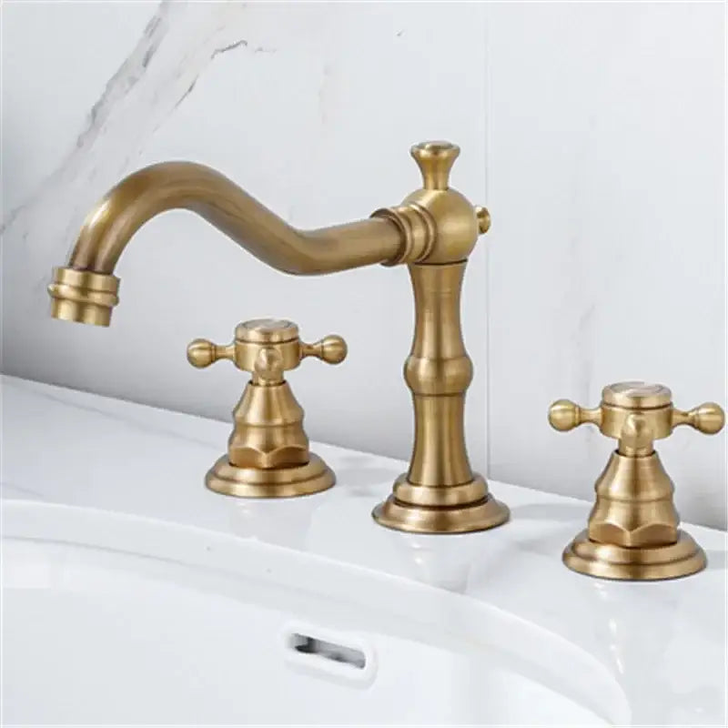 Antique brass gold finish three-handle bathroom sink faucet with ornate cross handles and a curved spout