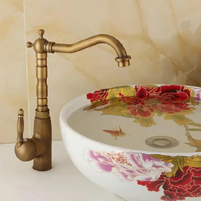 Antique brass ornate decorbites basin sink faucet beside white ceramic vessel sink with red and pink floral patterns