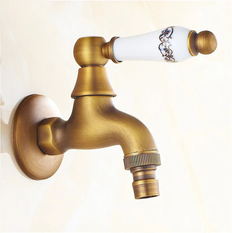 Antique brass single hole outdoor faucet with white ceramic handle black floral detailing and gold toned housing material