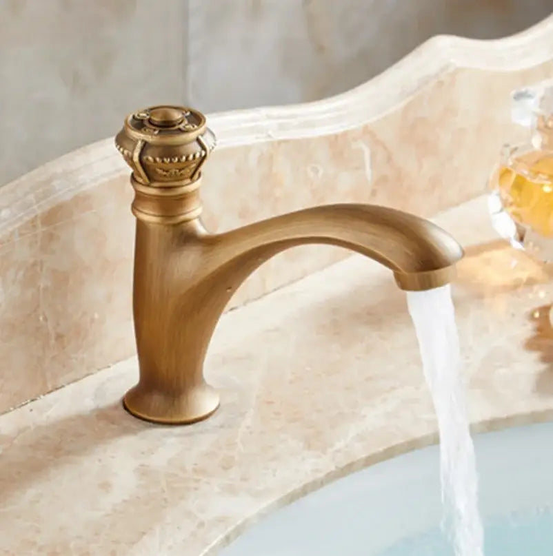 Antique brass single handle basin faucet with ornate crown-like knob and curved spout for bathroom use