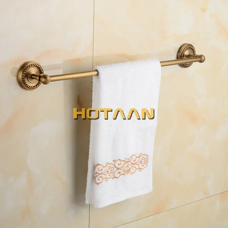 Antique brass single towel bar with ornate base holding a white towel with gold embroidered floral design in bathroom