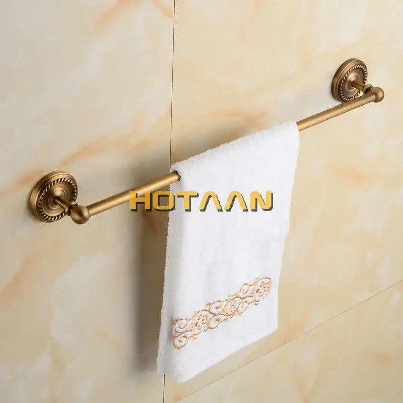 Antique brass single towel bar with ornate circular wall mounts holding a white embroidered single towel