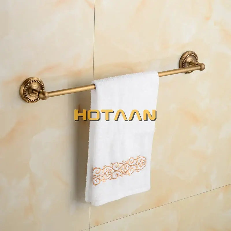 Antique brass single towel bar with ornate base holds a white towel with gold embroidery for bathroom decor