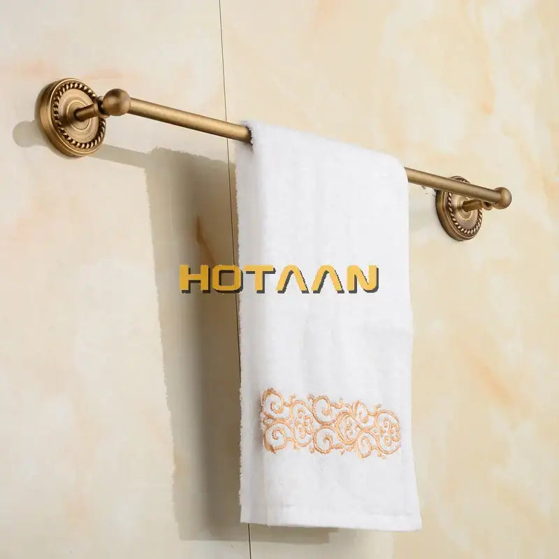 Antique brass single towel bar with ornate base holding a white towel with gold embroidery for bathroom decor
