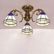 Antique brass three-arm semi flush mount ceiling fixture with blue and cream stained glass bell shades featuring geometric patterns