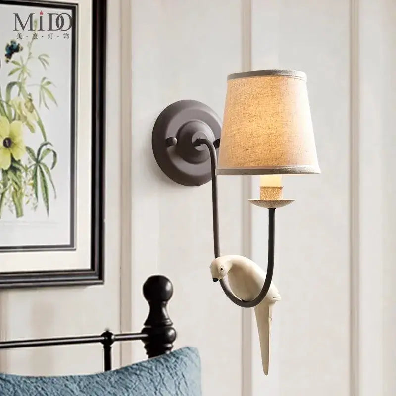 A cream ceramic parrot perches on an antique bronze wall lamp with beige linen shade bird decor decorbites bird decor