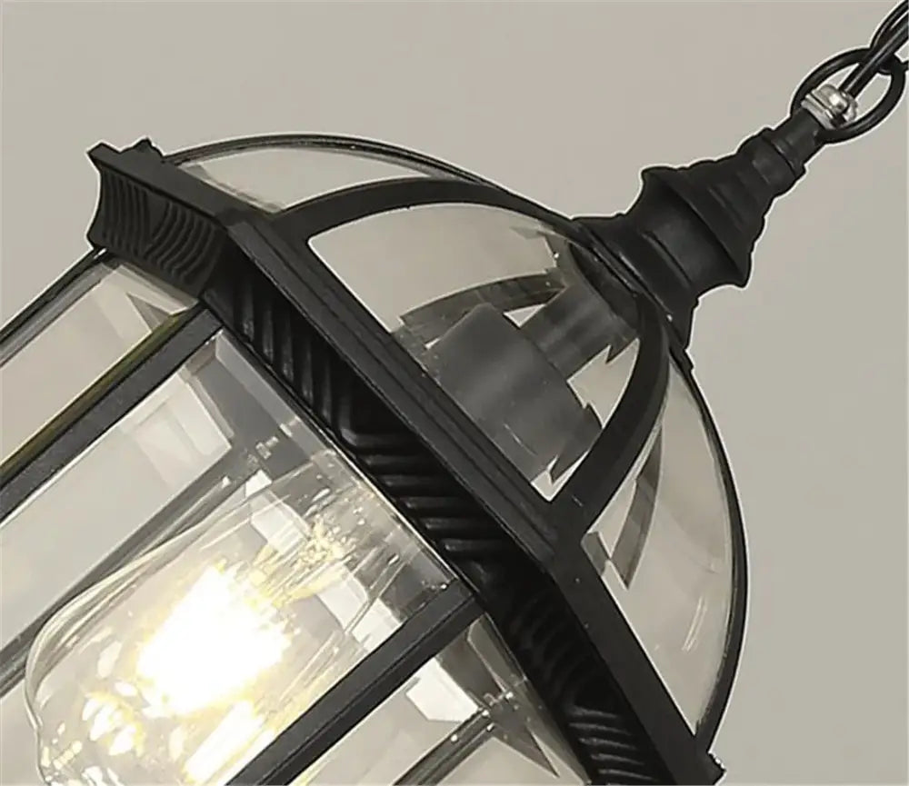 Antique bronze black outdoor hanging pendant light featuring a black wrought iron lantern with clear glass panels and filament bulb