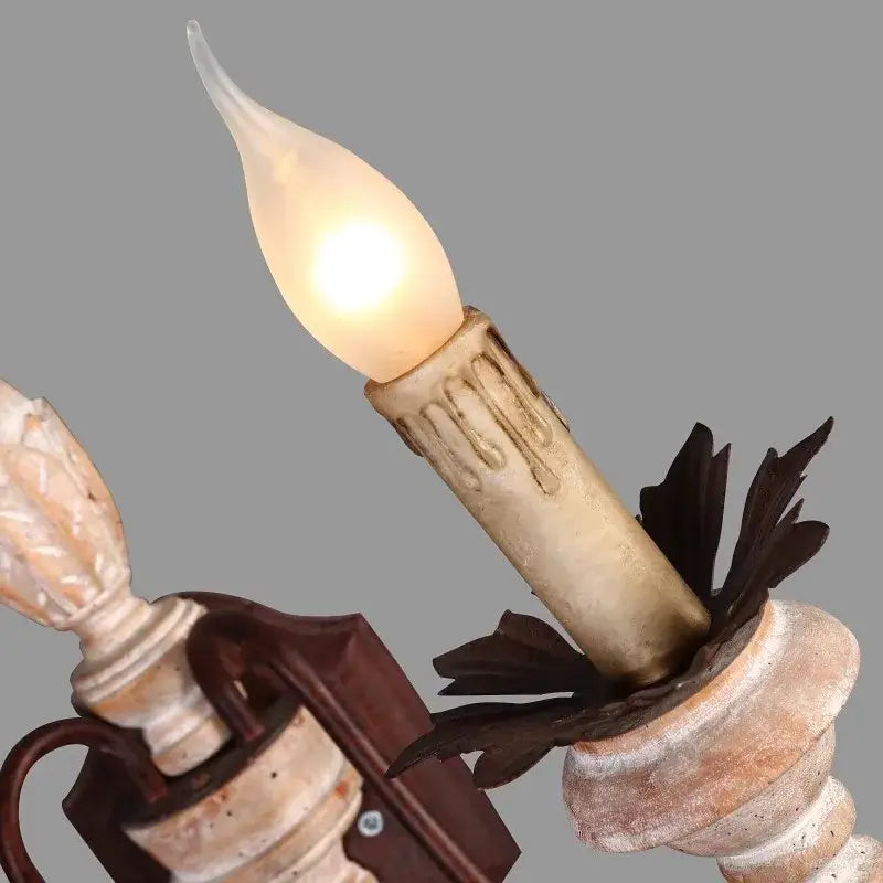 A warm glowing candle wall lamp with frosted glass on a distressed white double head french bedroom sconce