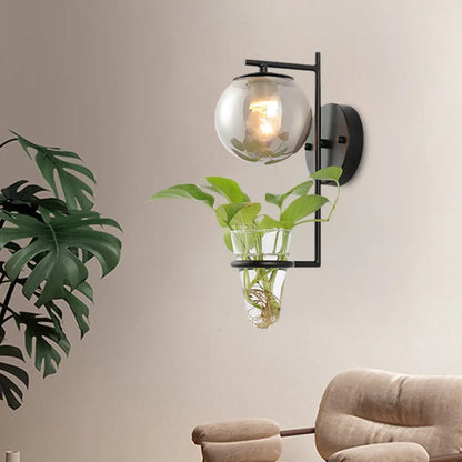 Aplique de pared antiguo dorado/negro con pantalla esférica y cristal crema/gris ahumado, lámpara de pared de una cabeza para dormitorio con maceta de cristal transparente.