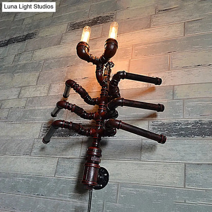 Aplique de pared estilo antiguo con forma de araña, dos bombillas y diseño rústico de tubería.