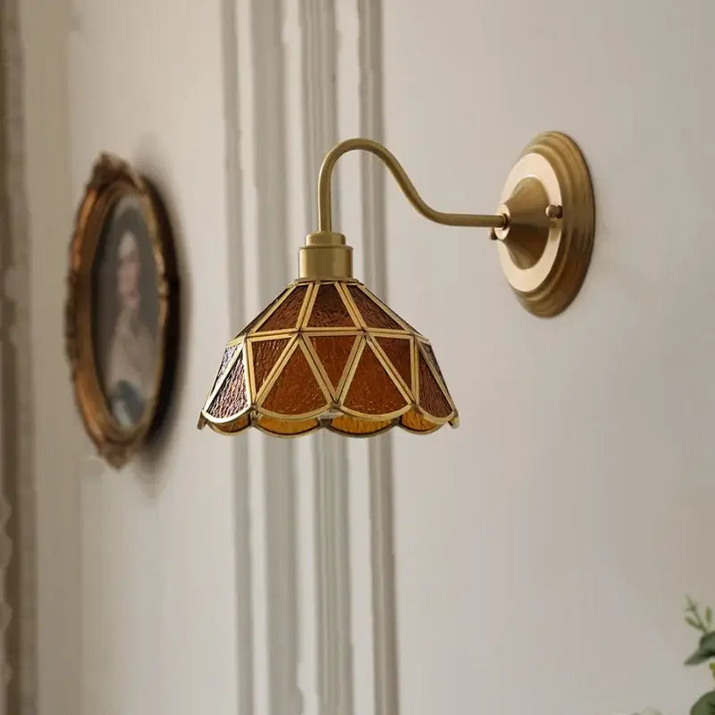 Antique brass wall light fixture with a geometric amber stained glass shade for bedroom use