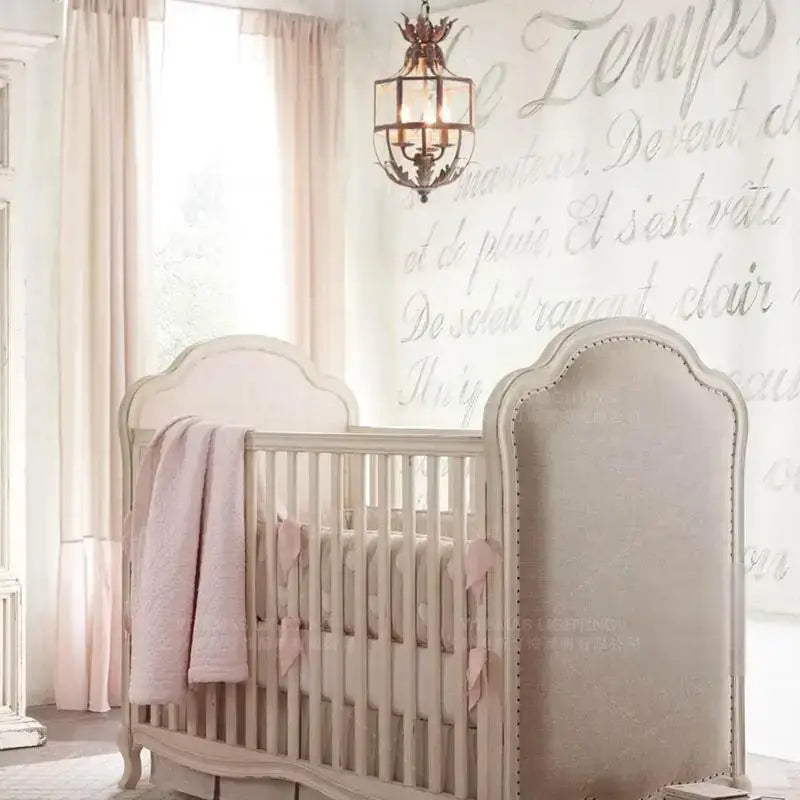 Beige upholstered crib with arched headboard and nailhead trim paired with decorbites elegant candle chandelier lights
