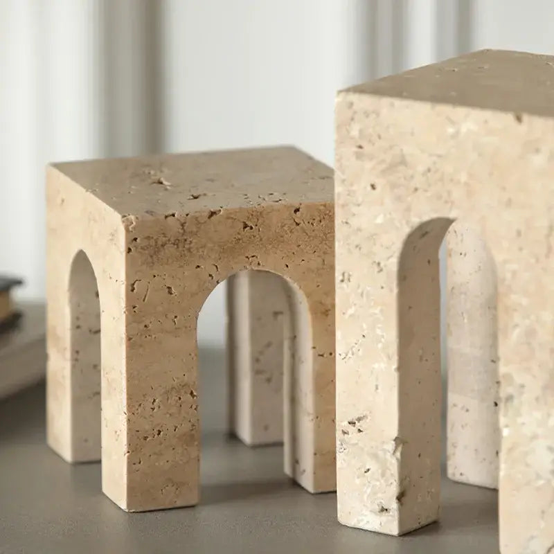 Beige stone bookends with arched cutouts and natural texture complement travertine coffee table cabinet designs