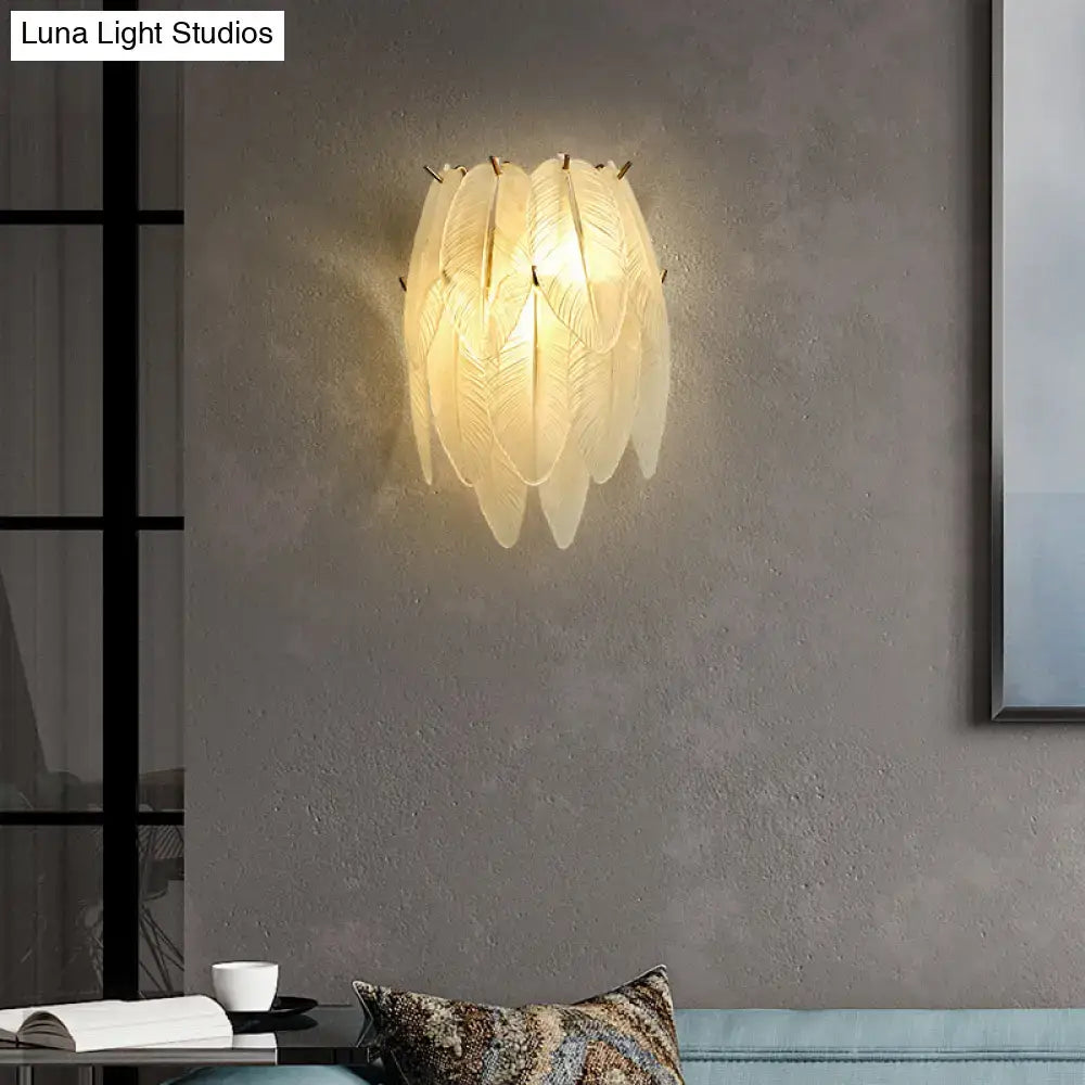Art deco brass leaf sconce lamp with clear glass and cream-colored feather design emitting a warm glow for dining room