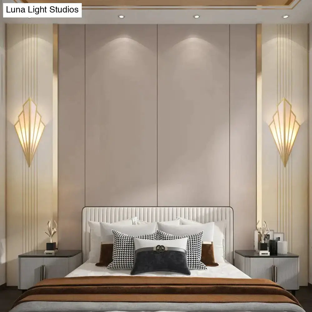 The bed with a white tufted headboard and plush pillows complements the art deco gold diamond shape modern wall light