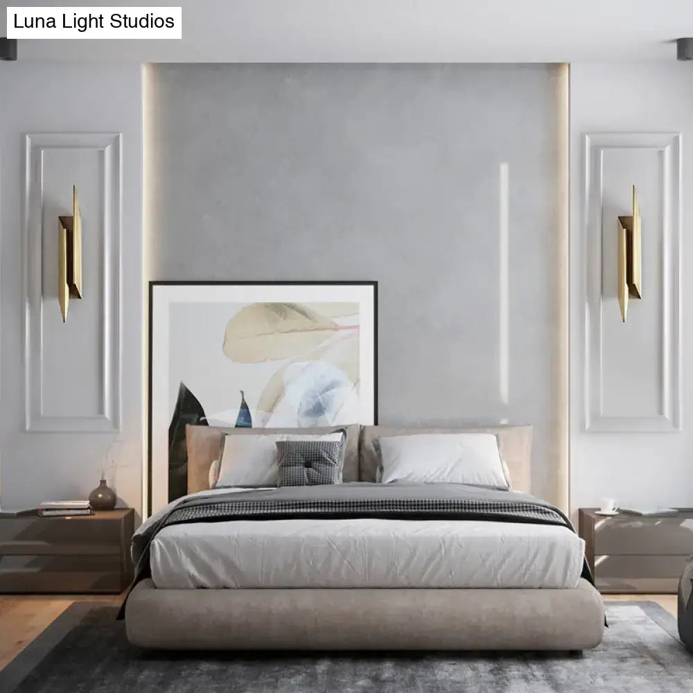 Modern gray upholstered bed with low-profile design and matching pillows beneath art deco gold geometric wall lamp sconce