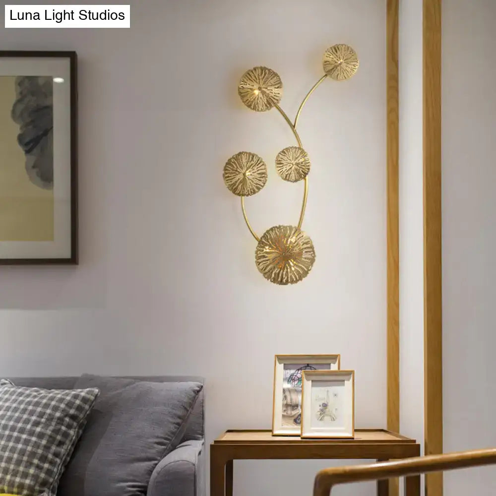 Gold-toned metal art deco wall mount light fixture with five detailed lotus shapes on a curved branch for bedroom use