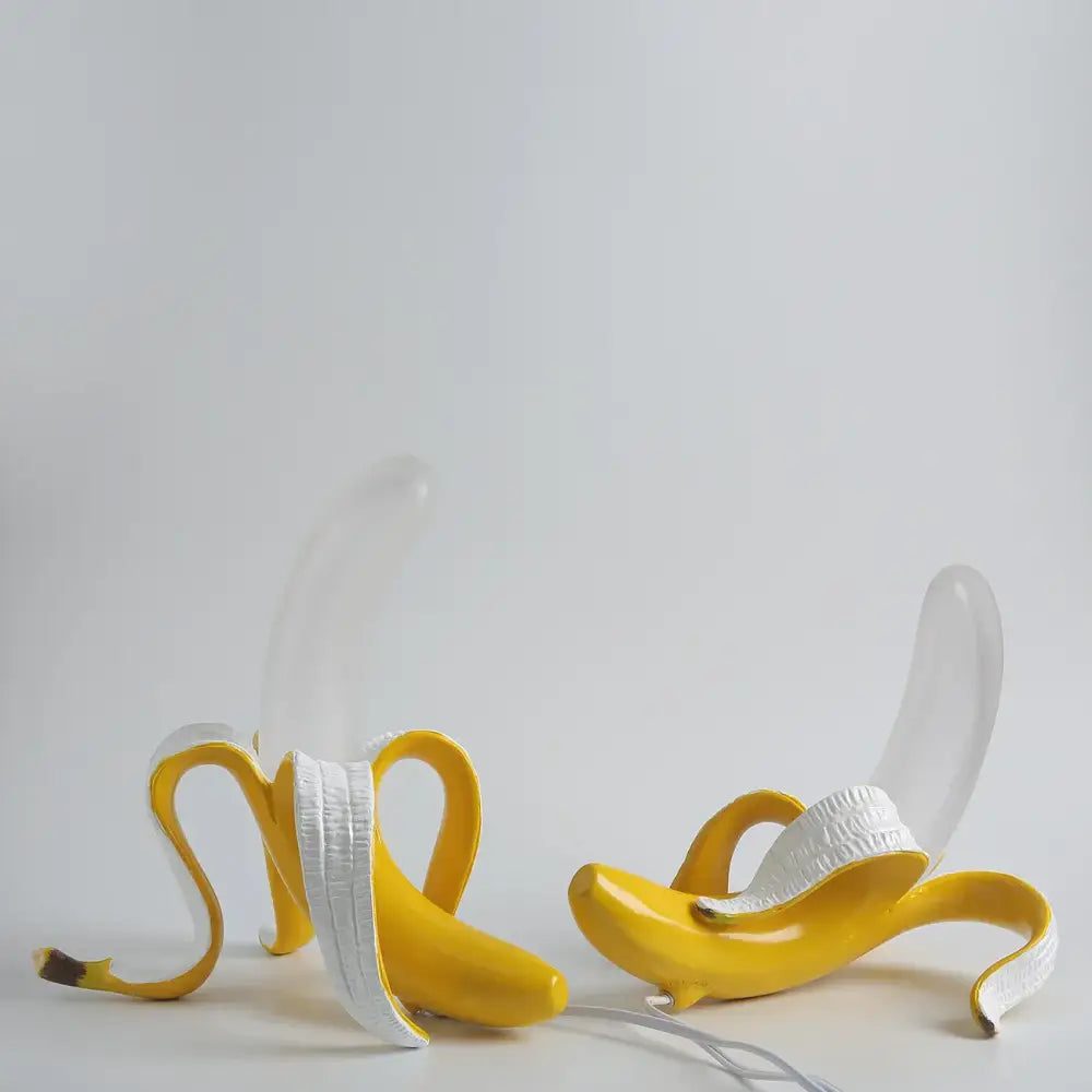 Two glossy yellow banana-shaped lighting fixtures with peeled white interiors and decorbites glass lampshade led stems