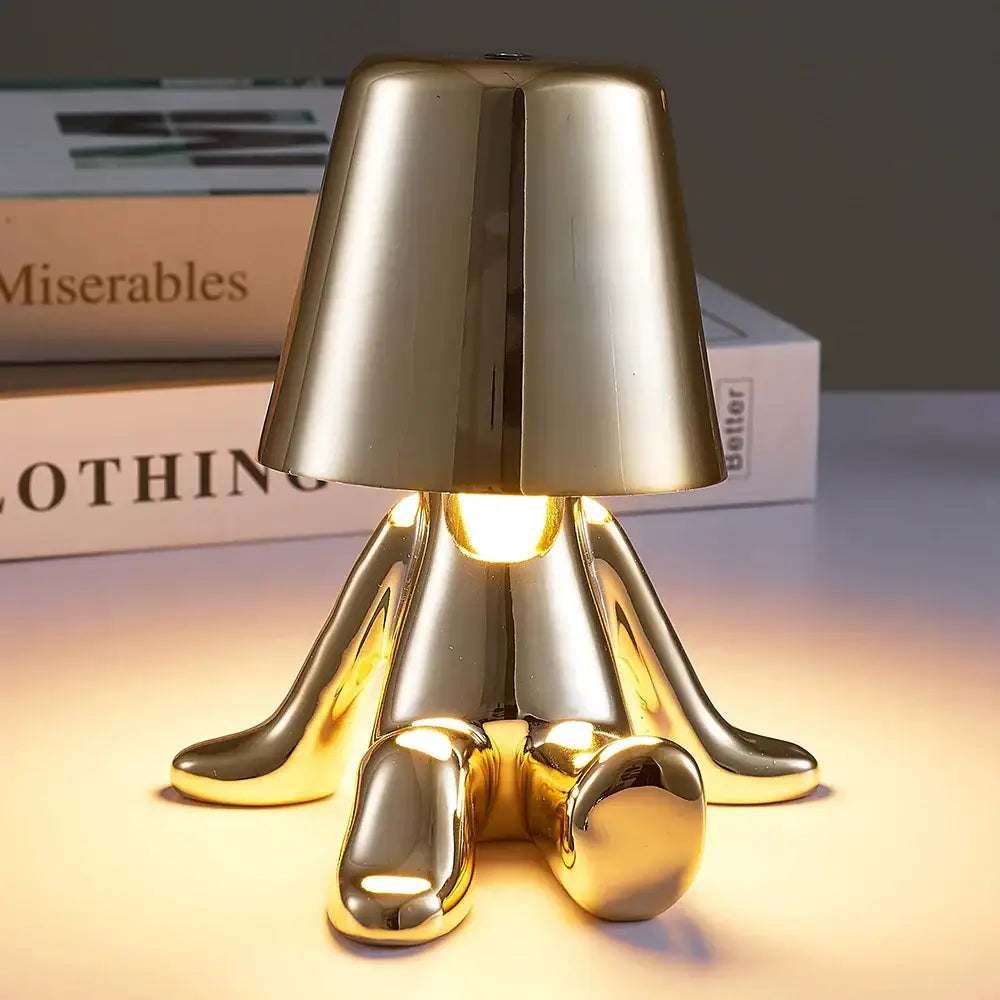 Golden metallic man table lamp with sleek minimalist design resembling a seated figure ideal as a bedroom night light
