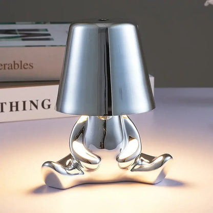Shiny silver metallic man table lamp shaped like a seated figure with bell-shaped shade for bedroom night light